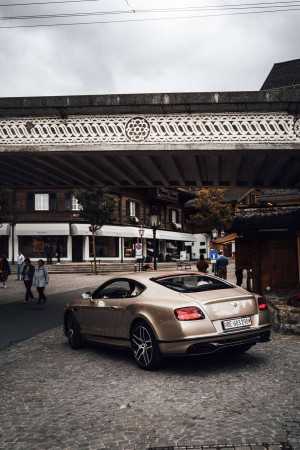 Bentley parked on a cobblestone street in a quaint European town with traditional architecture.