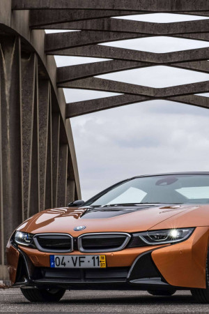 Front view of an orange BMW i8 sports car parked under a concrete bridge.