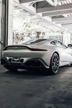 Rear view of a silver Aston Martin DB11 parked under a concrete structure.
