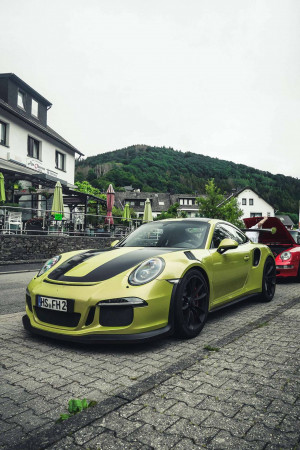 A vibrant lime green Porsche GT3RS parked on a cobblestone street with a scenic backdrop.