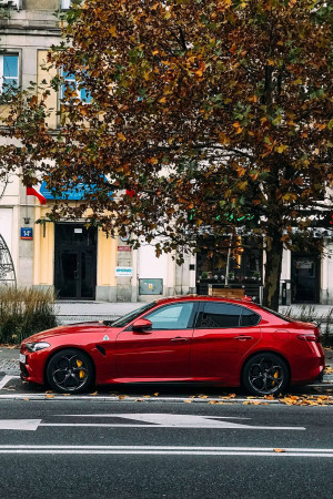 A red Alfa Romeo Giulia parked on a city street in autumn.