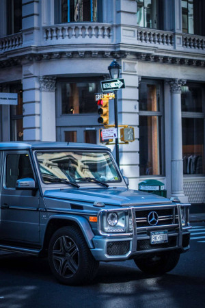 Silver Mercedes-Benz G-Wagon parked on a street in New York City with a one-way sign and traffic lights.
