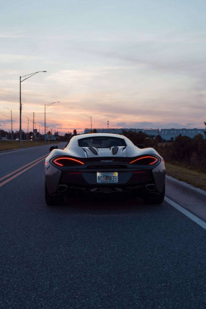 Rear view of a gray McLaren on a road at sunset