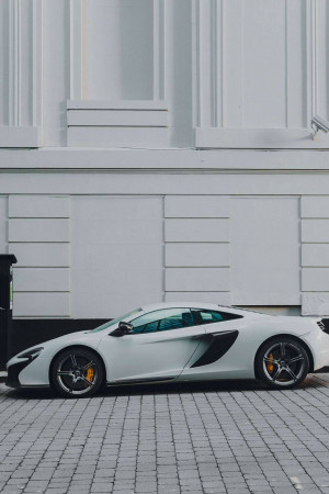 Side view of a white McLaren sports car parked on a brick street.