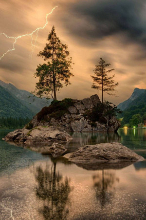 Dramatic lightning strike over a calm lake with trees and mountains.