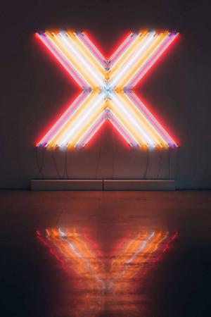A bright neon 'X' sign against a dark wall with a reflection on the floor.