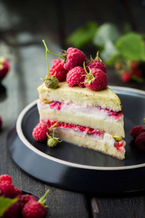 A close-up of a slice of raspberry layer cake on a dark plate.
