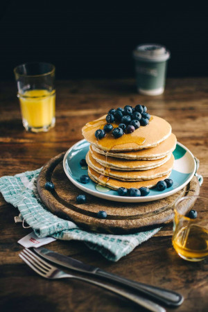 Stack of blueberry pancakes with syrup, orange juice, and coffee