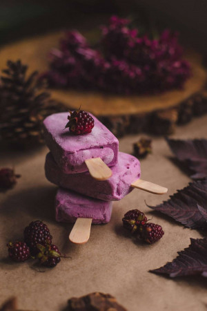 Stack of three purple raspberry popsicles with fresh raspberries and lilac flowers
