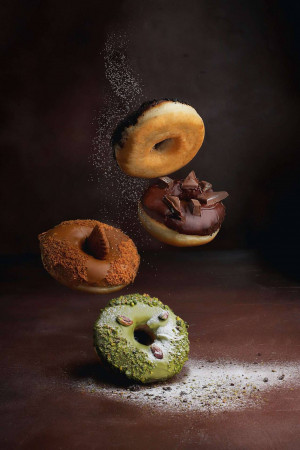 Three donuts in mid-air with powdered sugar, chocolate, and pistachio toppings.