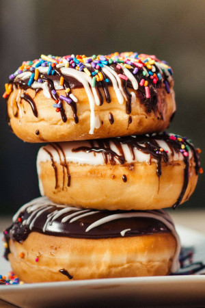 A close-up of a stack of three glazed and sprinkled donuts.