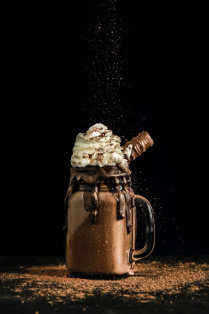 A close-up of a chocolate milkshake in a glass with whipped cream and chocolate sprinkles.