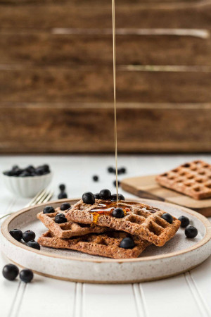 Stack of chocolate waffles drizzled with honey and topped with fresh blueberries
