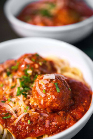 Close-up of spaghetti and meatballs in a red sauce, garnished with cheese and herbs.