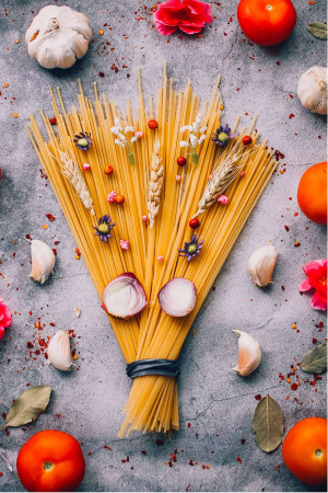 Overhead view of spaghetti, tomatoes, garlic, and other ingredients arranged on a grey surface.
