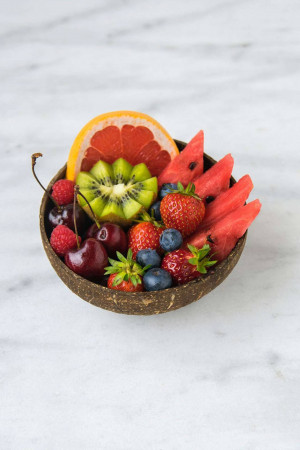 A bowl made of coconut shell filled with a colorful assortment of fresh fruits.