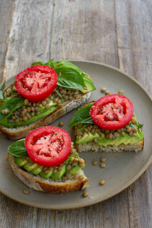 Close-up of toast topped with avocado, lentils, tomato, and basil.