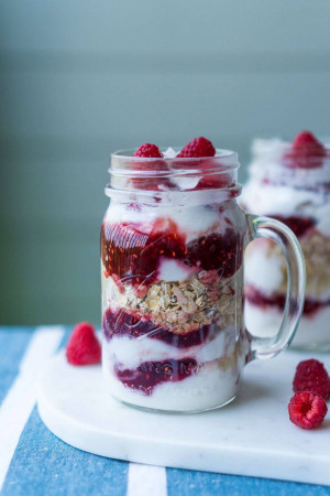 Close-up of a layered raspberry yogurt parfait in a mason jar with a handle, garnished with fresh raspberries.
