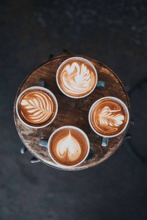 Overhead view of four lattes with beautiful latte art designs on a rustic wooden surface.