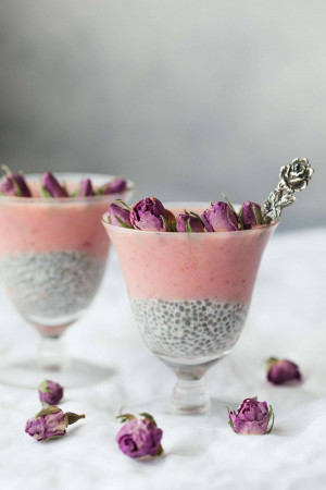 Two glasses of pink and black chia seed parfait topped with rose petals