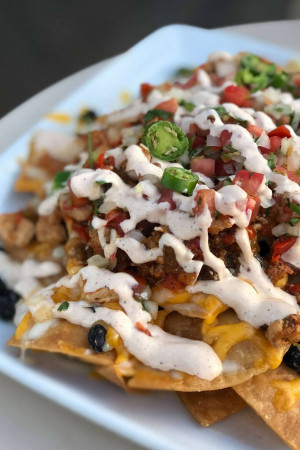 Close-up of a plate of loaded chicken nachos with cheese, beans, jalapenos, and a creamy sauce.