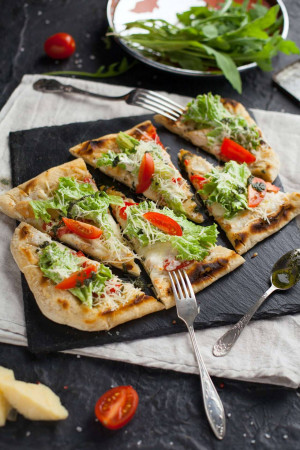 Close-up of bruschetta pizza slices on a slate board with fresh ingredients