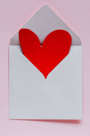 Red heart shaped paper coming out of a white envelope on a pink background