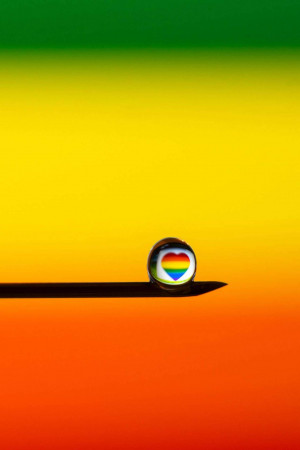 A water droplet reflecting a rainbow and heart shape, casting a shadow on a gradient background.