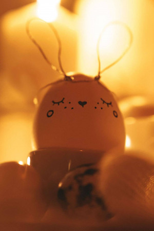 Close-up of a white egg decorated as a bunny face surrounded by blurred lights.