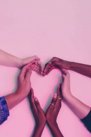 Diverse hands coming together to form a heart shape on a pink background.
