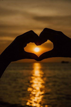 Silhouette of hands making a heart shape with a sunset in the background