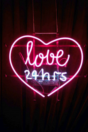 A neon sign in the shape of a heart with the word 'love' written inside and '24hrs' below it.