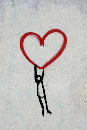 A black stick figure appears to be holding up a red spray-painted heart.