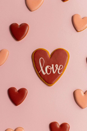 A flat lay of heart-shaped cookies in varying shades of red and pink on a pink background.