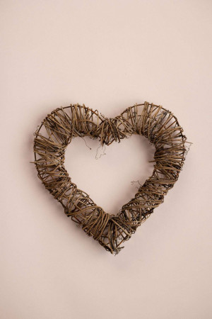 A heart-shaped wreath made of woven twigs and branches against a pale pink background.