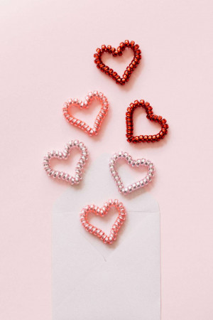 Close-up of several small beaded hearts in various shades of pink and red arranged on a white surface.