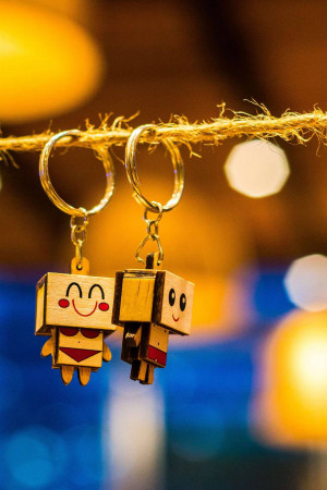 Two wooden robot-shaped keychains hanging from a string with a blurred bokeh background.