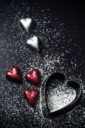 Close-up of chocolate hearts and a heart-shaped cookie cutter on a dark surface with powdered sugar.