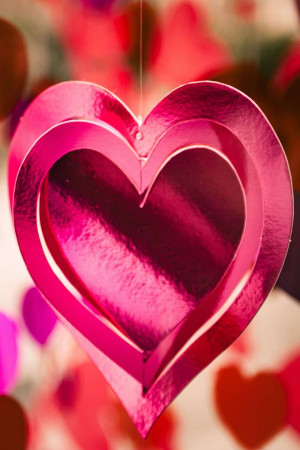 Close-up of a layered pink heart-shaped decoration hanging in front of a blurred background of hearts.