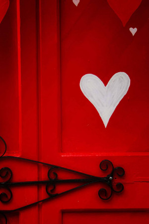 A close-up of a bright red door with a large white heart painted on it.