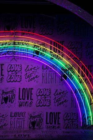 A vibrant neon rainbow archway with the words 'Love' and 'Live' repeated on a textured wall.