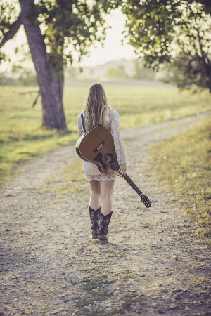 Woman walking away with a guitar on a dirt road