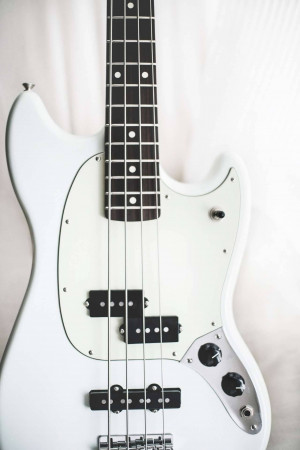 Close-up of a white Fender Precision Bass guitar against a white background
