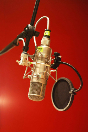Close-up of a professional studio microphone with shock mount and pop filter against a red background.