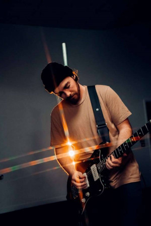 A young man playing an electric guitar on stage with dramatic lighting.
