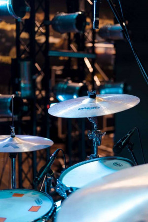 Close-up of a drum kit with cymbals and microphones on a stage with blue lighting.