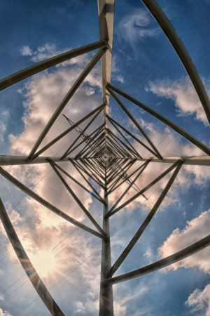 Low-angle view of a geometric metal structure against a cloudy blue sky.