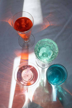 Overhead view of four colorful cocktail glasses with liquid inside, casting vibrant shadows.