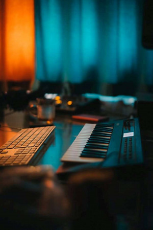 A dimly lit music production studio with a keyboard, midi controller, and computer equipment.