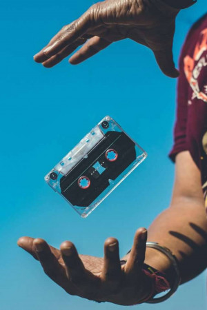 A person's hands holding a levitating cassette tape against a bright blue sky.